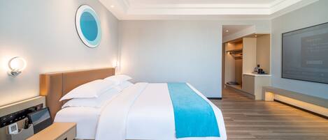 A modern hotel room with a large bed, bedside tables, a TV, and a bathroom visible in the background.