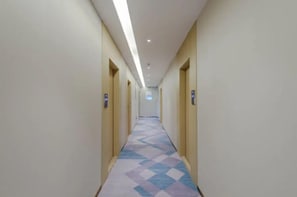 Un pasillo de hotel con alfombra estampada, puertas a ambos lados y una lámpara en el techo.