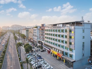 A multi-story hotel with a service apartment section, a parking lot, and a street view with cars and palm trees. - POLTTON SERVICE APARTMENT (Guangzhou Panyu Chimelong Nancun Branch) (Guangzhou)