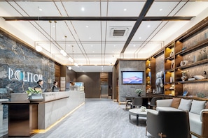 A hotel lobby with a reception desk, seating area, and a TV screen. - POLTTON SERVICE APARTMENT (Guangzhou Panyu Chimelong Nancun Branch) (Guangzhou)