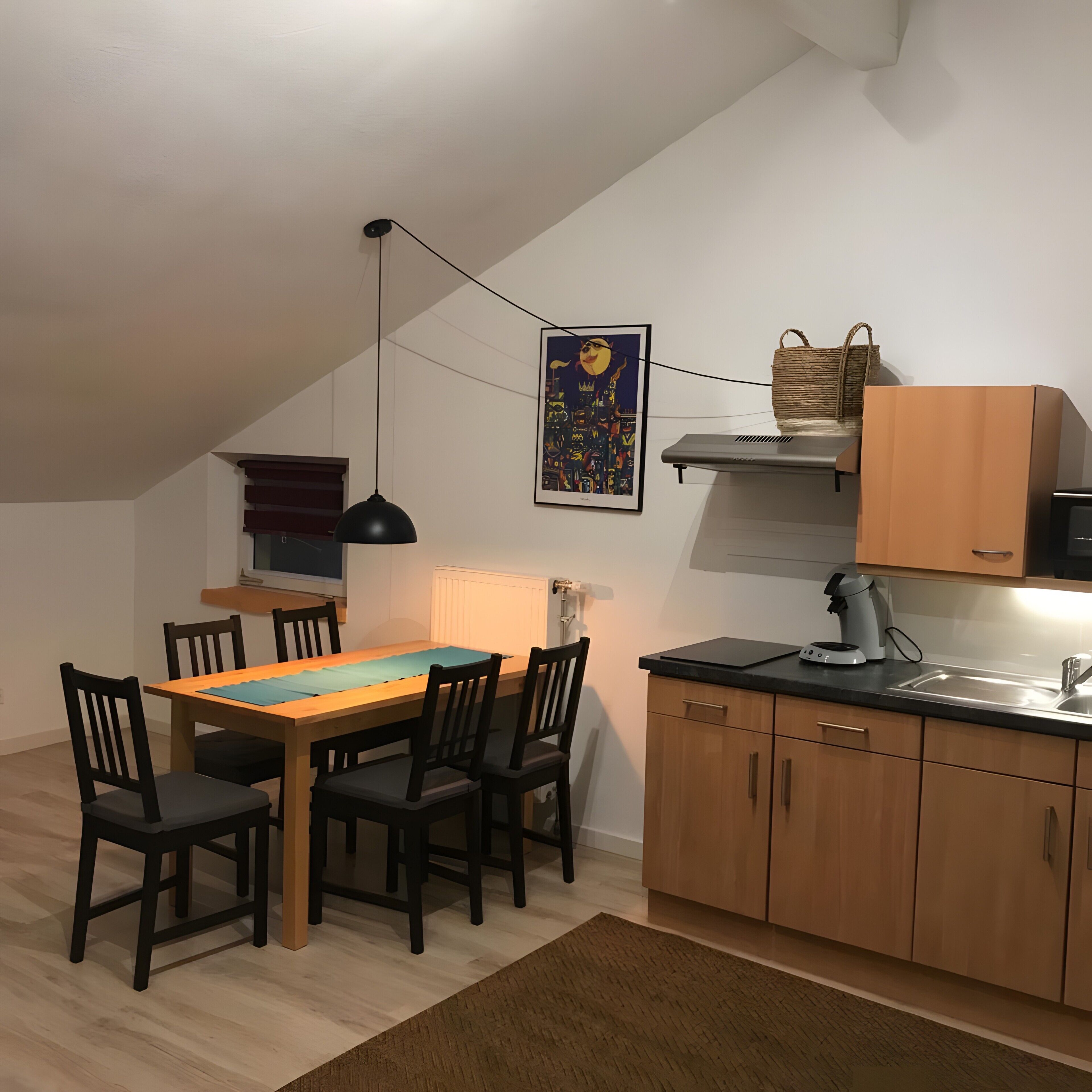 A dining area with a table and chairs, a kitchen with cabinets and a countertop, and a hanging light fixture.