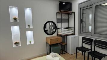 A modern bedroom with a bed, a desk, two chairs, a radiator, and a window with blinds.
