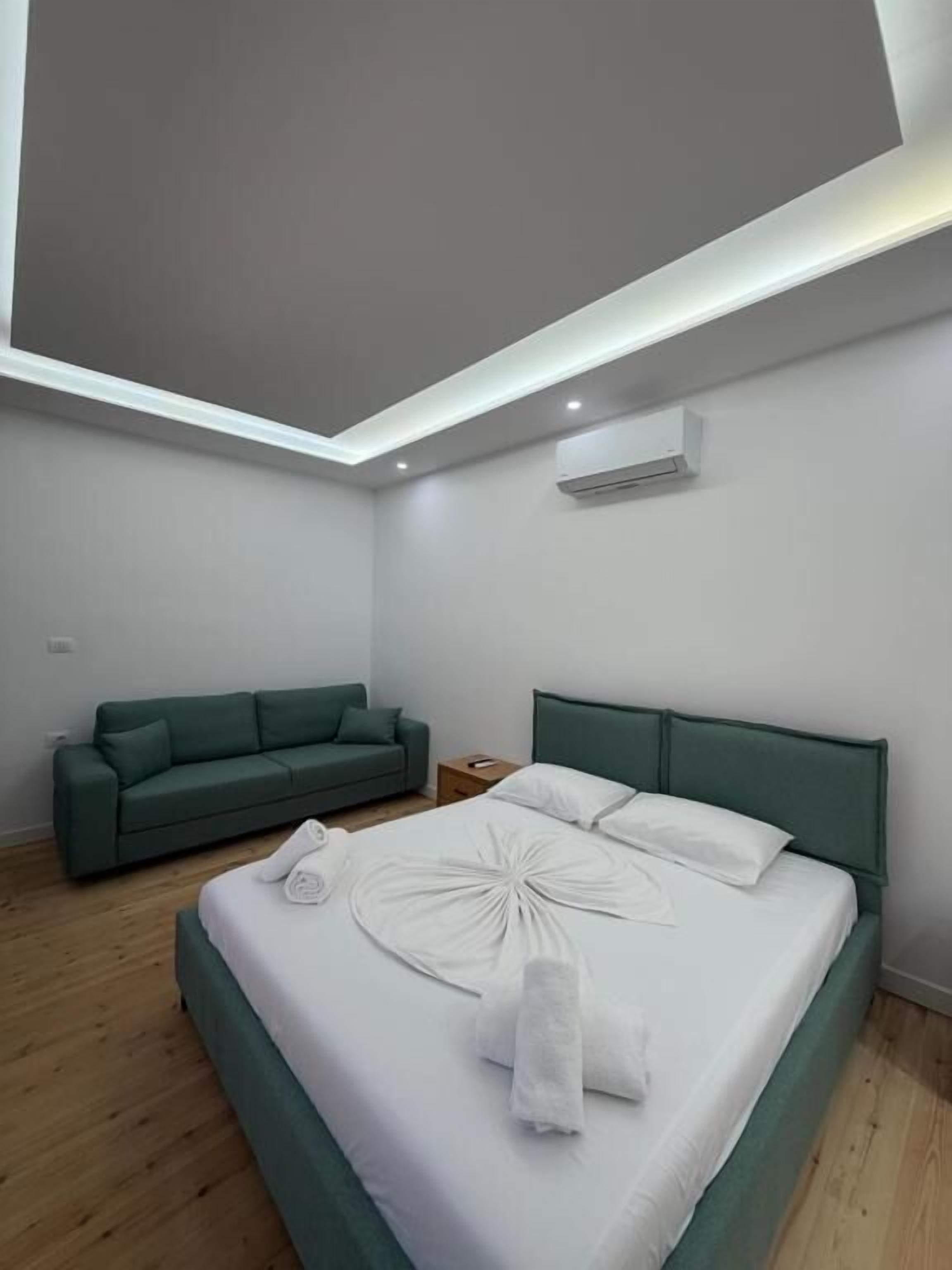 Una camera d'albergo moderna con un letto, un divano verde e una lampada a sospensione.
