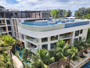 Un hôtel moderne à plusieurs étages, doté d’une piscine sur le toit et d’une végétation luxuriante.