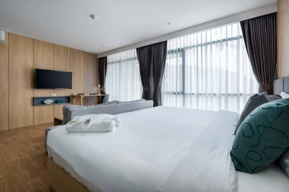 Quarto de hotel moderno com uma cama grande, televisão de tela plana na parede e uma janela com cortinas.