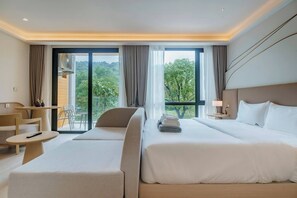 Une chambre d’hôtel avec un lit, un canapé, une petite table et une chaise. Il y a une fenêtre avec des rideaux et une vue sur les arbres.