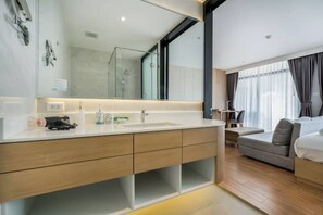 A modern bathroom with a large mirror, a sink, and a shower. There is a sofa and a bed in the adjacent room. - Sea Heaven Naithon Beach by Tropiclook (Thalang District)