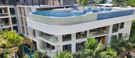Un hotel moderno con múltiples balcones, piscina en la azotea y exuberante jardinería tropical.