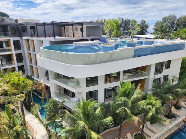 Un hôtel moderne doté de nombreux balcons, d’une piscine sur le toit et d’un aménagement paysager luxuriant de style tropical.