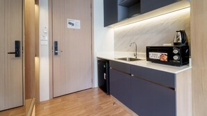 Een kleine keuken met een magnetron, spoelbak en een deur met een nooduitgangsbord.