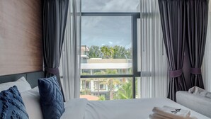 Hotelkamer met een groot bed, twee kussens, een raam met gordijnen en uitzicht op gebouwen en bomen.