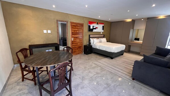 Una habitación de hotel moderna con cama, sofá, mesa de comedor con sillas y un televisor pequeño.