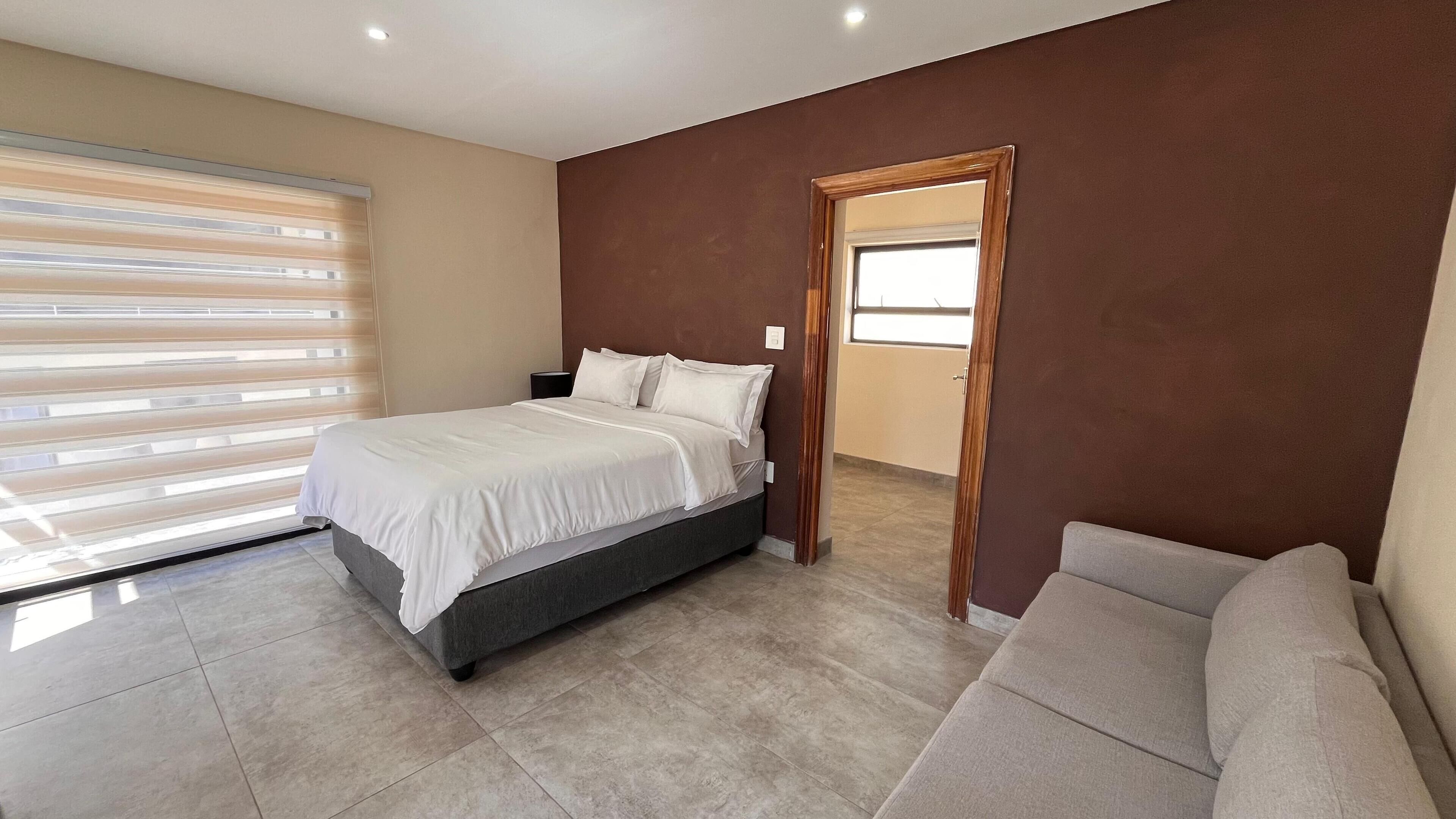 Une chambre à coucher avec un lit, un canapé, une fenêtre avec des stores et une porte.
