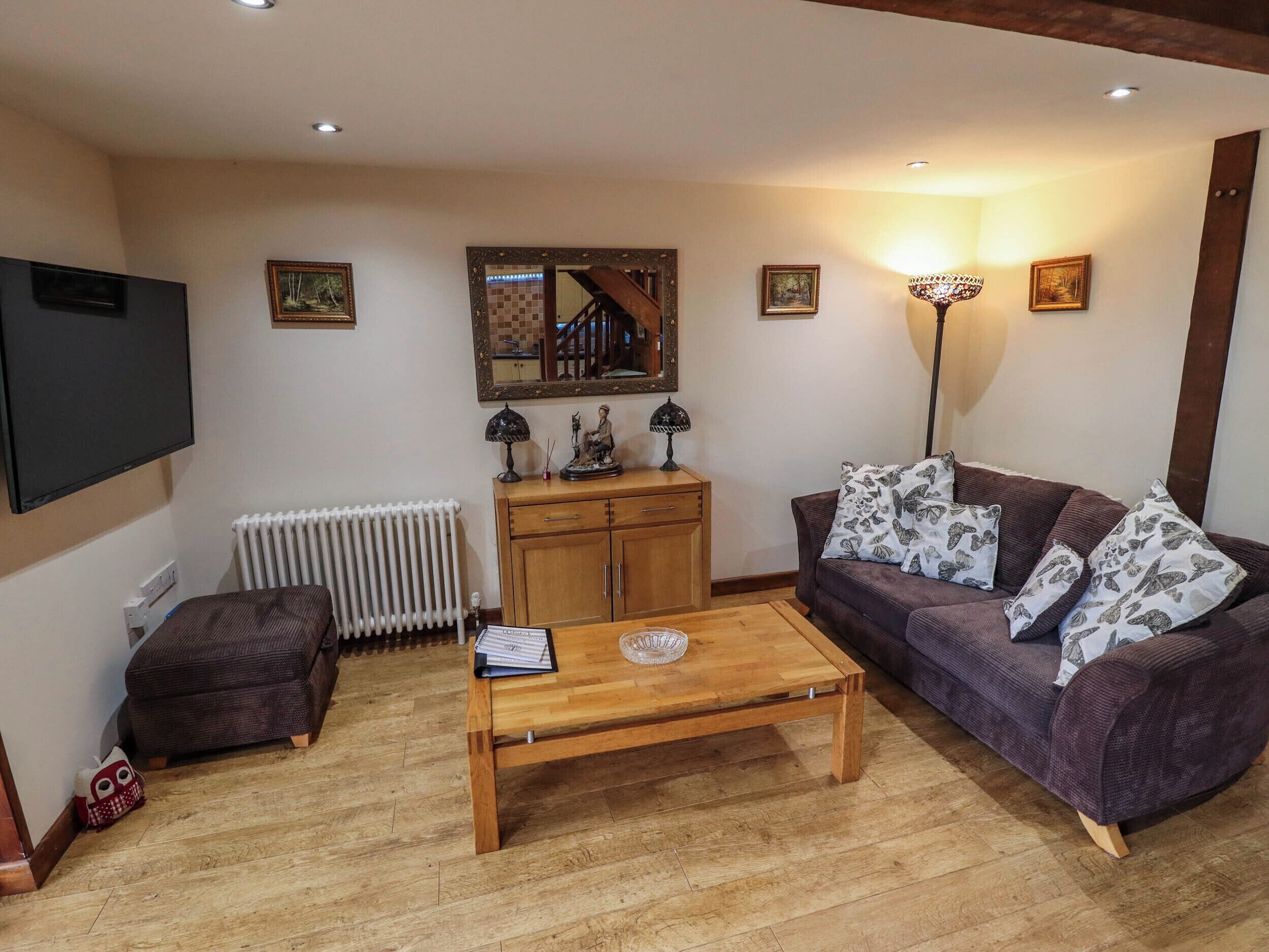 A living room with a sofa, a coffee table, a TV, a radiator, a wooden cabinet, and a mirror.