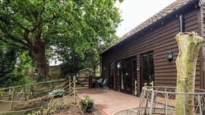 A rustic wooden building with a covered patio area, a metal spiral bench, and a large tree in the background.
