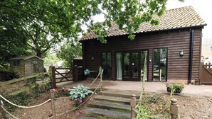 A wooden building with a tiled roof, a wooden deck with a rope barrier, and a small garden area with flowers.