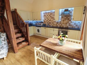 A kitchen with wooden cabinets, a washing machine, a dining table with chairs, and a staircase.
