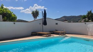 En swimmingpool med klart, blåt vand, omgivet af en hvid mur, samt en bænk og en parasol.