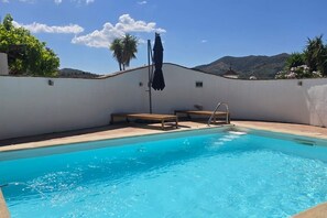 A swimming pool with a clear blue water, surrounded by a white wall, with a bench and an umbrella. - Andalusian villa, private pool & mountain views (Loma las Chozas)