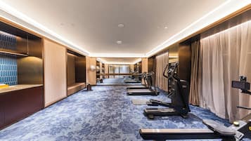 A hotel fitness room with exercise equipment, a blue patterned carpet, and wooden walls.