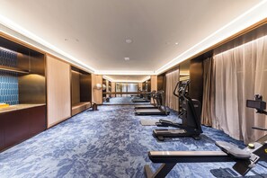 A hotel fitness room with exercise equipment, a blue patterned carpet, and wooden walls.