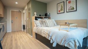 Ein modernes Schlafzimmer mit Bett, Nachttisch und Blick auf einen Flur, der zu einem Badezimmer führt.