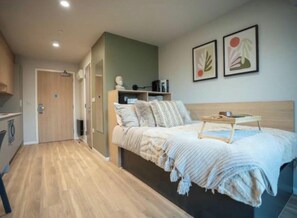 A modern bedroom with a bed, bedside table, and a view of a hallway leading to a bathroom. - Student Only Fusion York (York)