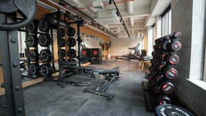 Ein Fitnessstudio mit Geräten für das Krafttraining, Laufbändern und einem an der Wand befestigten Hantelständer.
