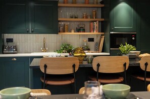 A modern kitchen with dark cabinetry, a central island with chairs, and a microwave. - Student Only Fusion York (York)