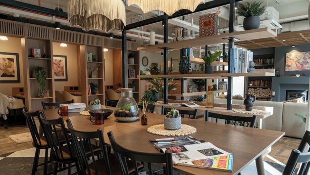 Ein modernes Interieur mit einem Holztisch, schwarzen Stühlen und Regalen mit Büchern und Pflanzen.