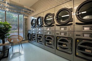 A laundry facility with multiple washing machines, a chair, and a potted plant. - Student Only Fusion York (York)