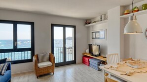 Een kamer met uitzicht op zee, een rieten stoel, een bureau met een computer en een eettafel.