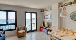 A room with a view of the sea, a wicker chair, a desk with a computer, and a dining table. - Seafront apartment (Calella de Palafrugell)