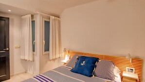 Een slaapkamer met een bed, nachtkastje, lamp, raam met gordijnen en een deur.
