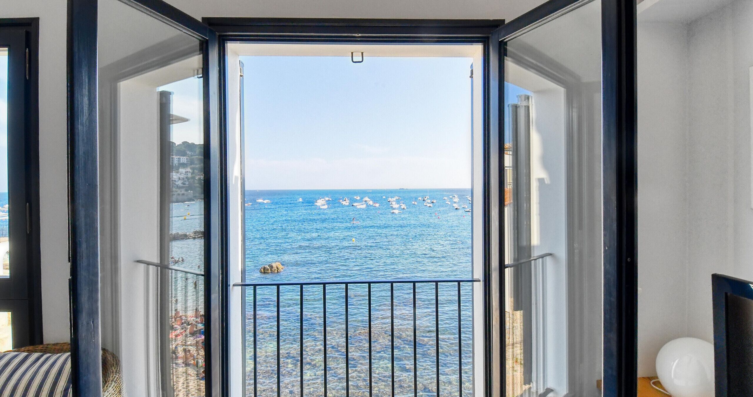 A room with a view of the sea, a balcony with a railing, and a window with a view of boats.
