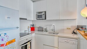 Een compacte keuken met witte kastjes, een magnetron, een spoelbak en een Bosch vaatwasser.