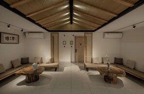 A modern interior with wooden ceiling beams, two sofas with cushions, and two round tables with vases. - JIDMI HOTEL (Xiamen)