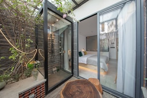 A modern bedroom with a glass door leading to a balcony, a wooden bench, and a small plant. - JIDMI HOTEL (Xiamen)