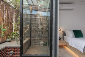 A modern room with a glass shower enclosure, a bed with white bedding, and a small bedside table. - JIDMI HOTEL (Xiamen)