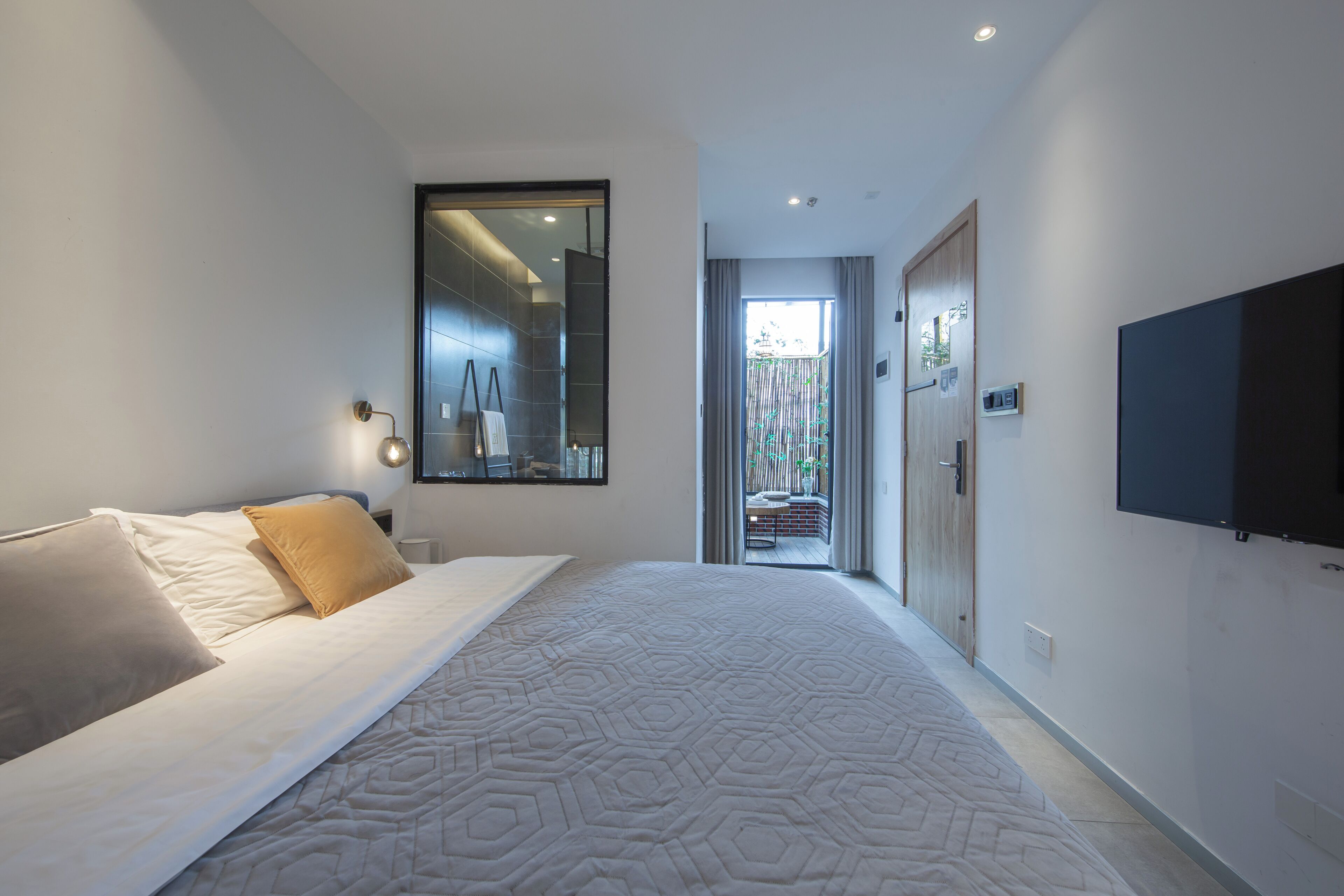 Un dormitorio moderno con una cama grande, un televisor montado en la pared y vistas al exterior.