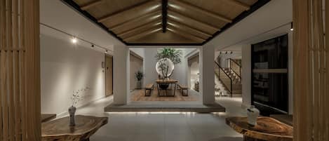 A spacious interior with a high ceiling, wooden beams, a central table with benches, and a staircase.