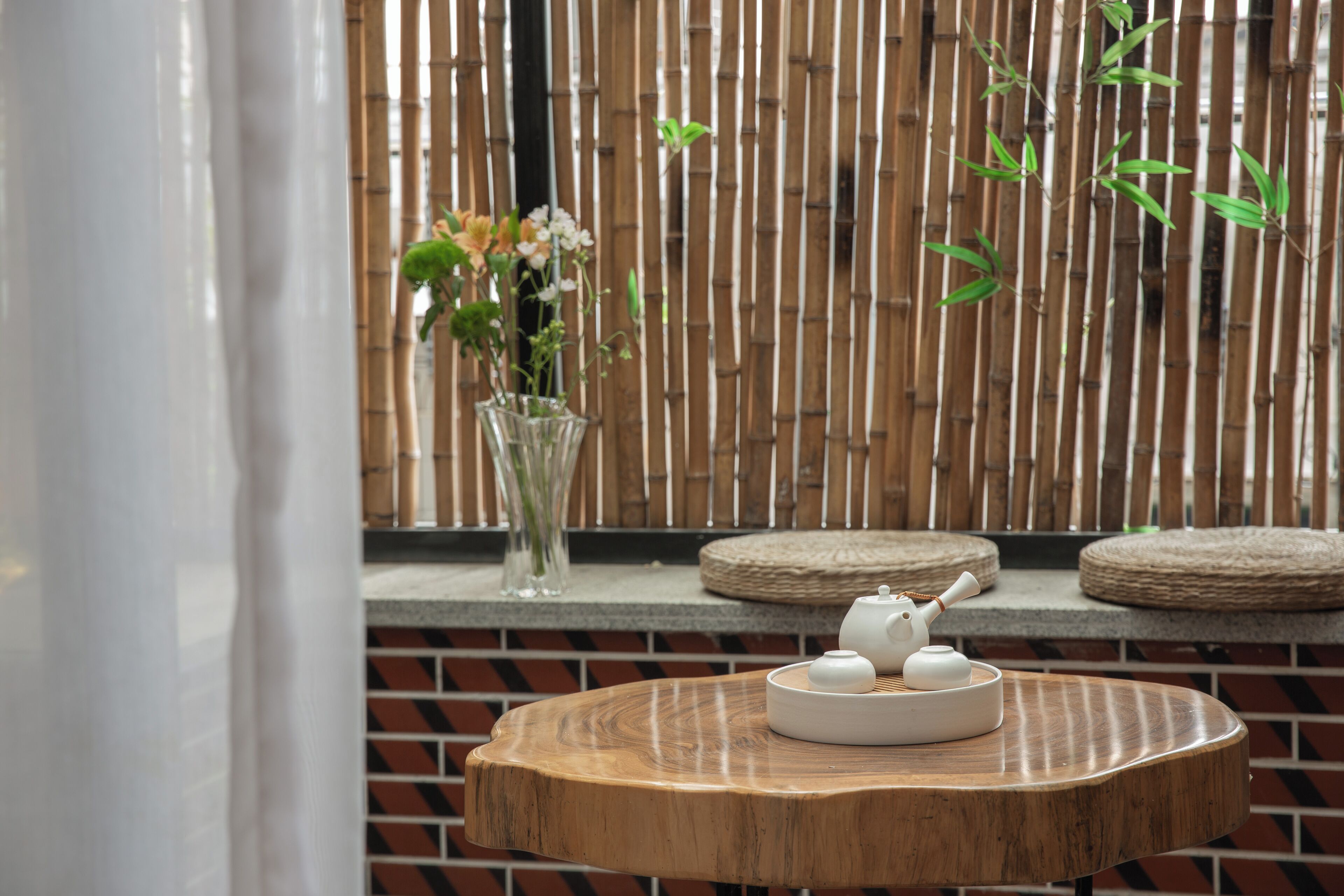 A wooden table with a teapot and cups, a vase with flowers, and a bamboo backdrop.