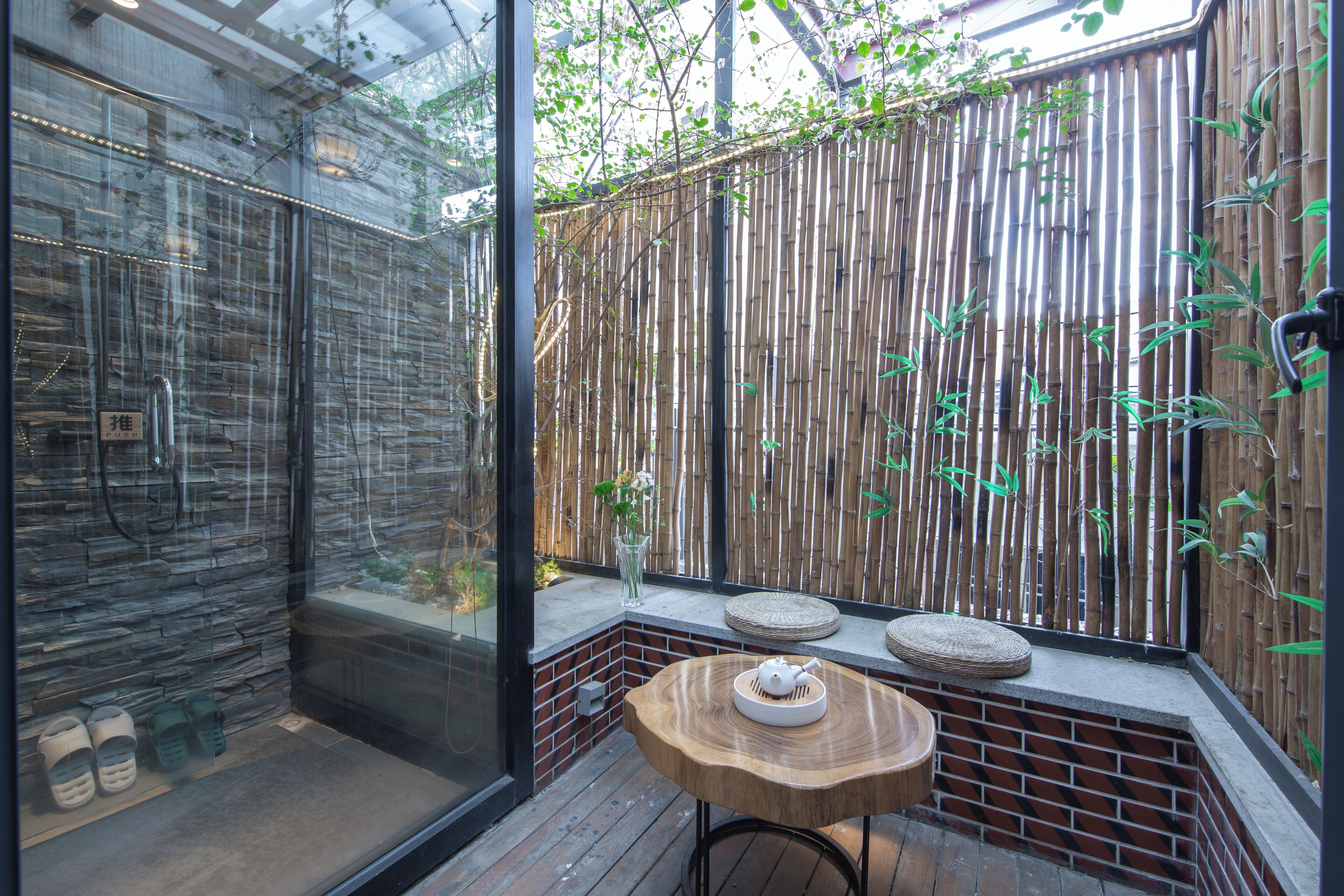 Une salle de bain moderne avec une douche en verre, un mur en bambou et une petite table en bois sur laquelle est posée une théière.