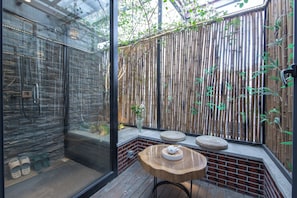 A modern bathroom with a glass shower enclosure, a bamboo wall, and a small wooden table with a teapot. - JIDMI HOTEL (Xiamen)