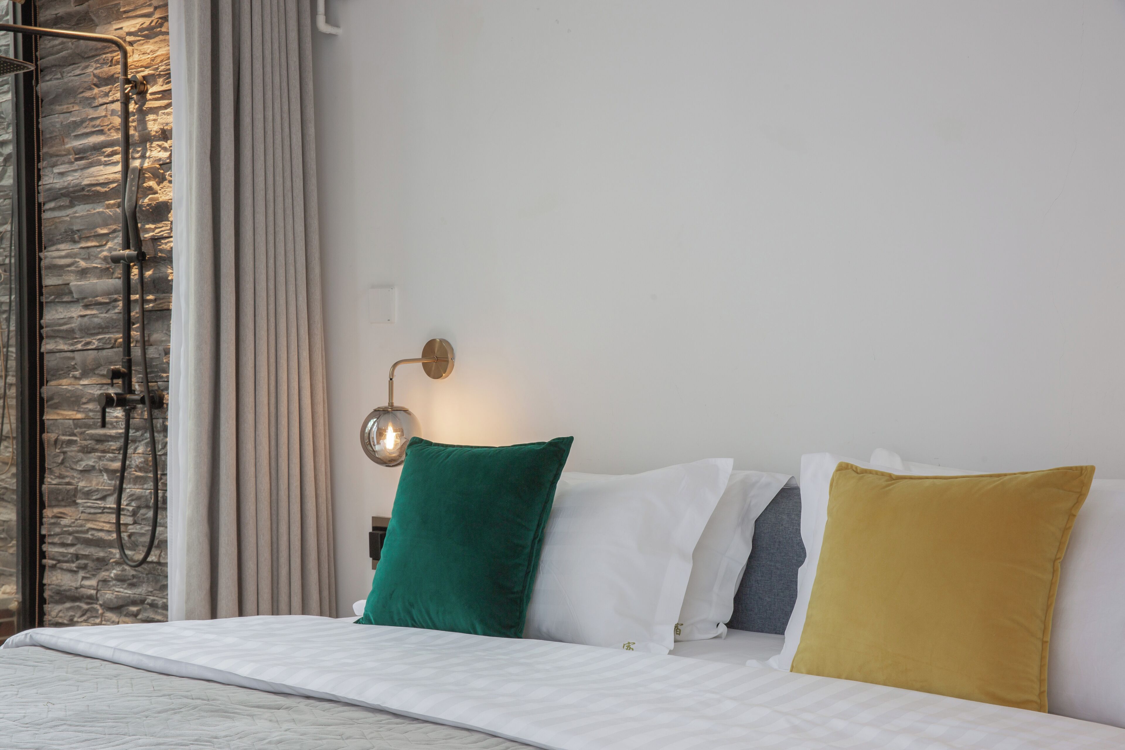 A neatly made bed with a white quilt, a green pillow, and a yellow pillow.
