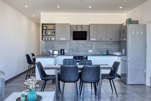 Une cuisine moderne avec des meubles gris, un four encastré et un coin repas comprenant une table et des chaises.