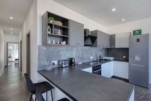 A modern kitchen with a central island, built-in appliances, and a first aid kit. - Gozo Sannat Penthouse 3BDR (Sannat)