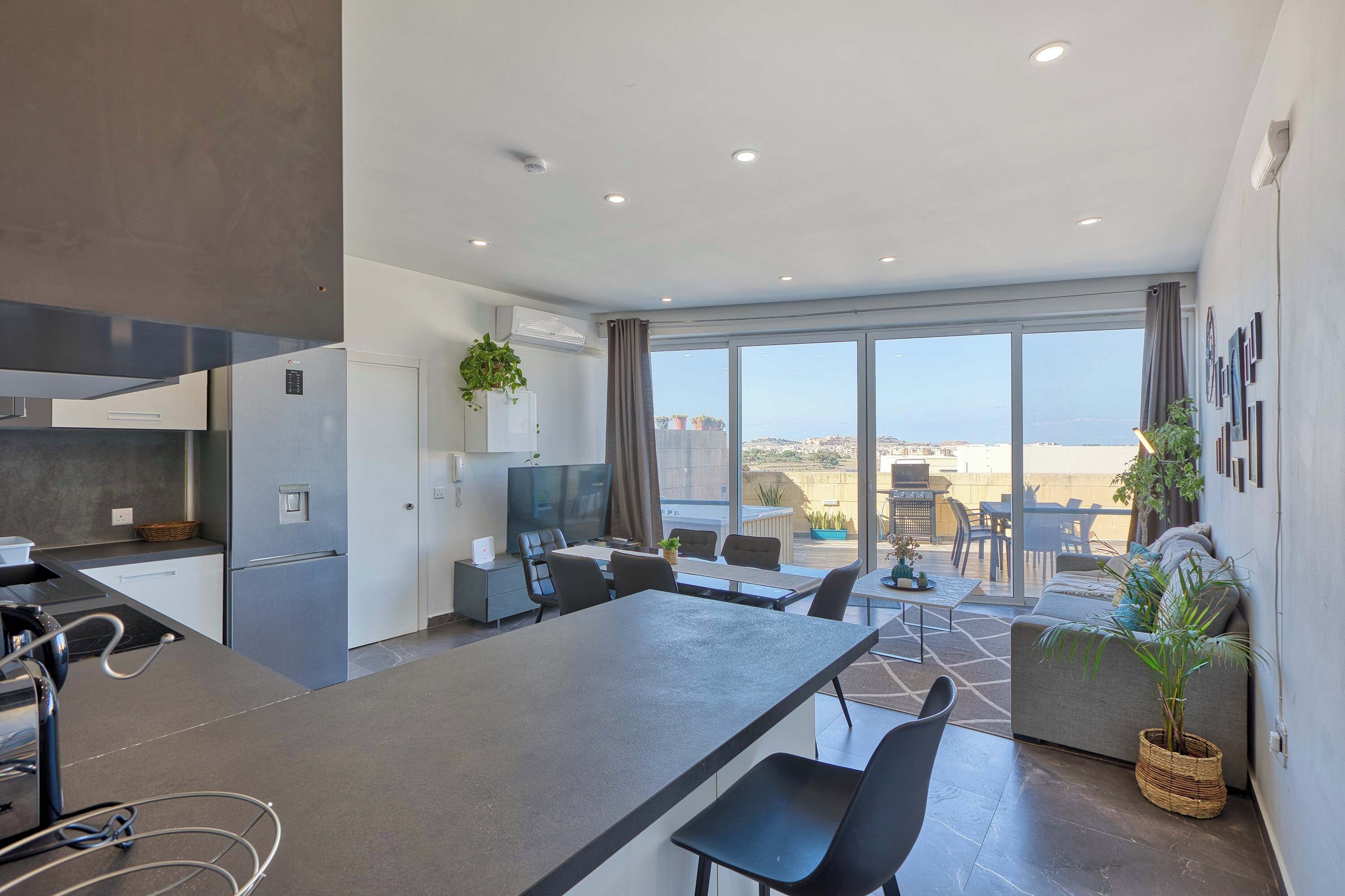 A modern kitchen with a central island, dining area with chairs, and a view of the city through large windows.