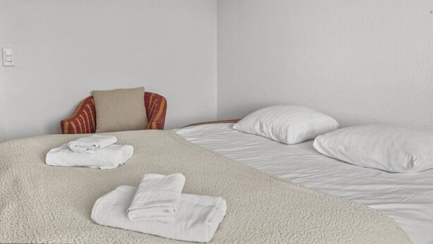 Quarto de hotel com cama, duas almofadas, uma cadeira com enchimento estampado e toalhas dobradas na cama.