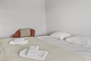 Hotellihuone, jossa on sänky, kaksi tyynyä, kuviollisella päällisellä varustettu tuoli ja sängylle taitellut pyyhkeet.